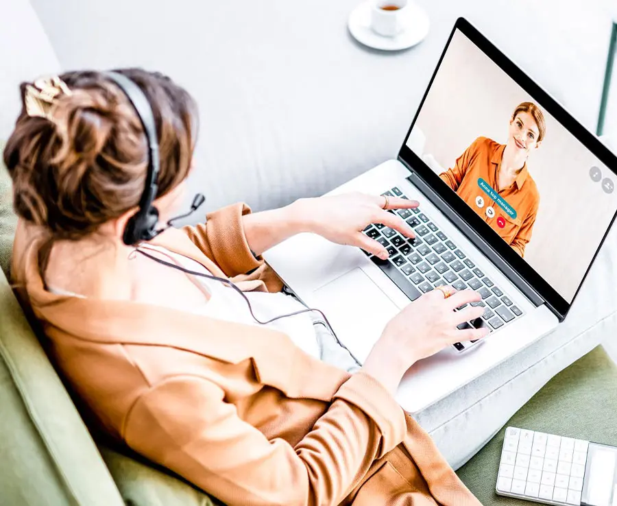 karriere tutor® Frau mit Headset führt über einen Laptop ein Videogespräch mit einer anderen Frau; in der Nähe steht eine Tasse Kaffee und eine Tastatur.