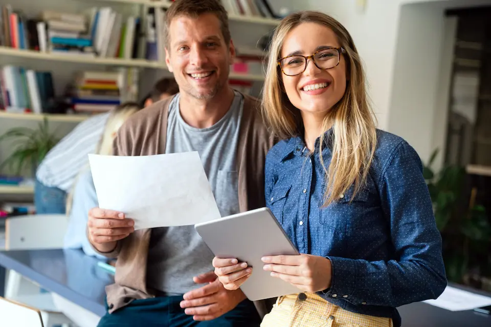 karriere tutor® Zwei lächelnde Menschen sitzen in einem Büro mit Bücherregalen im Hintergrund.